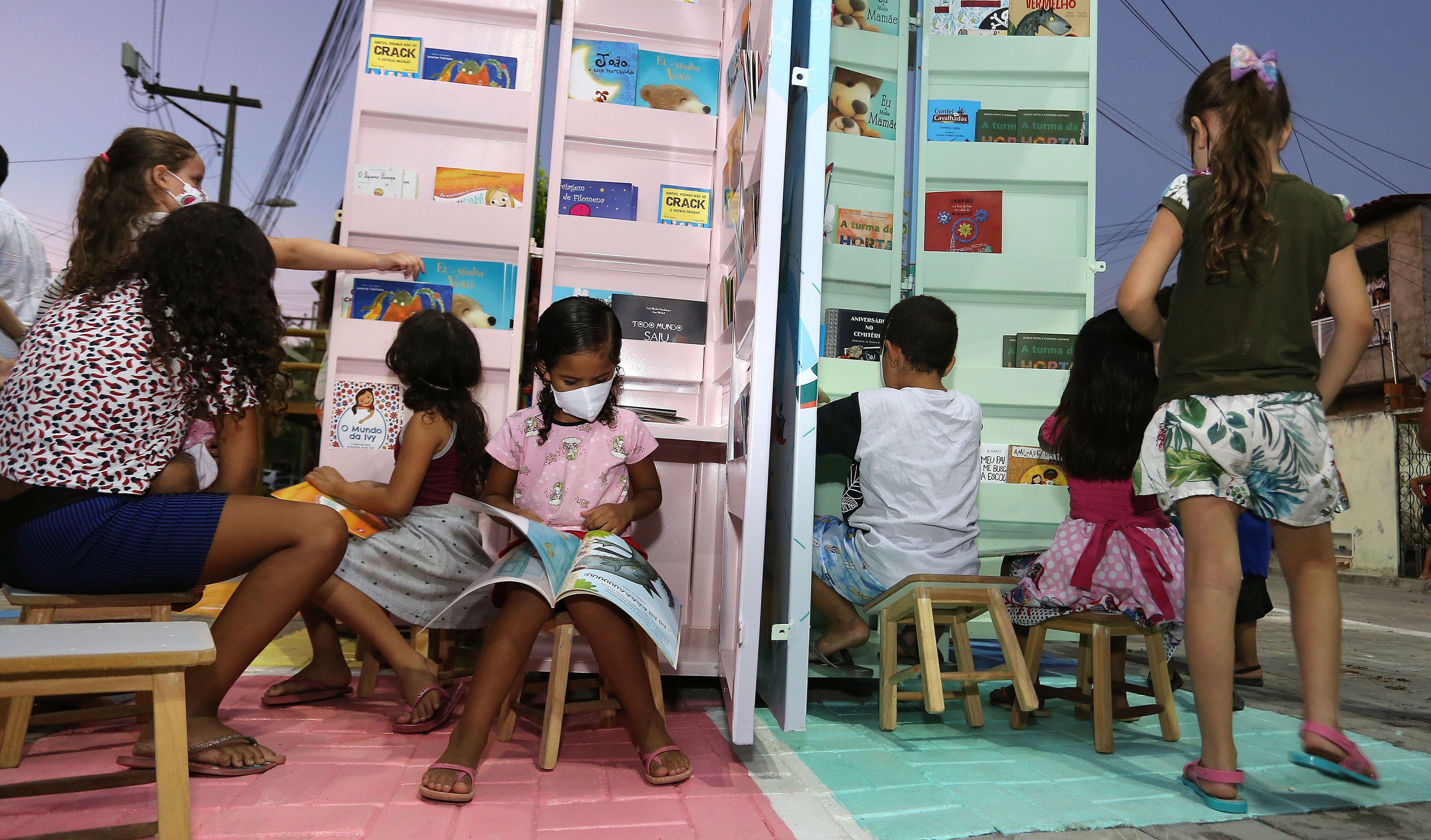 crianças lendo livros em um quiosque montado na praça